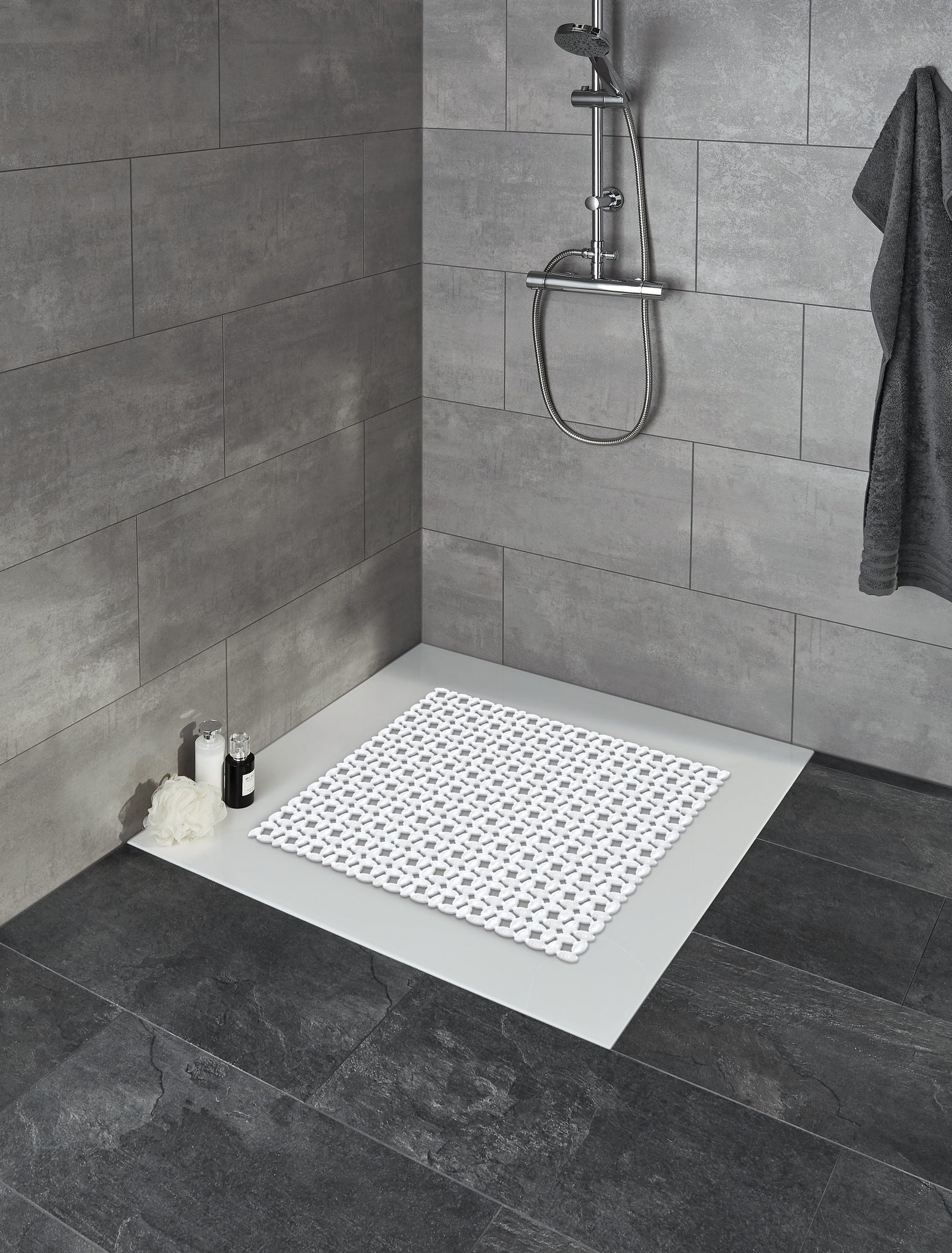 Duscheinlage IVY Weiß 54x54 cm liegt in moderner Dusche mit grauen Fliesen und Duschgelflaschen.
