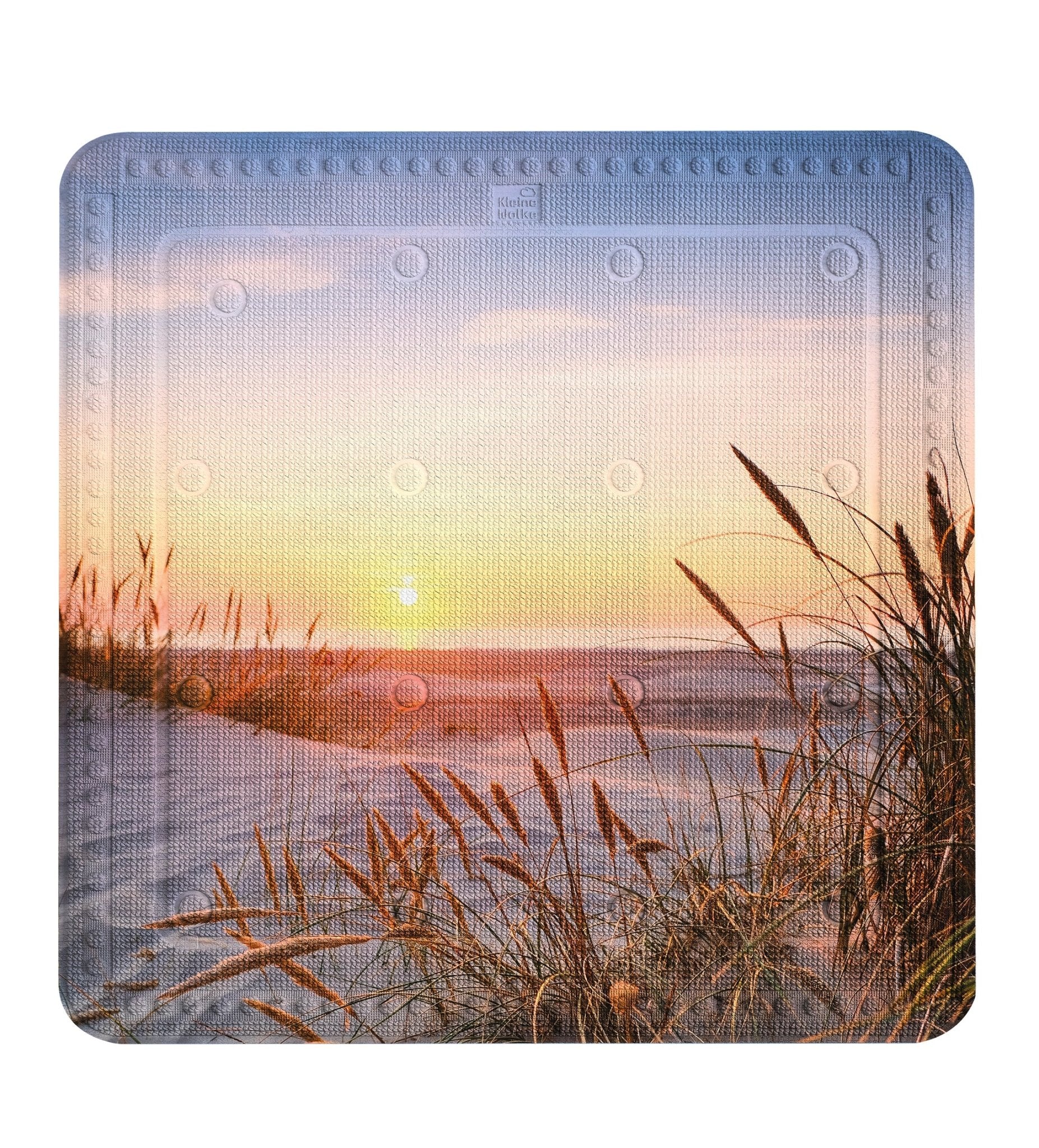 Badematte mit Sonnenuntergang am Strand und Gräsern in den Dünen vorne