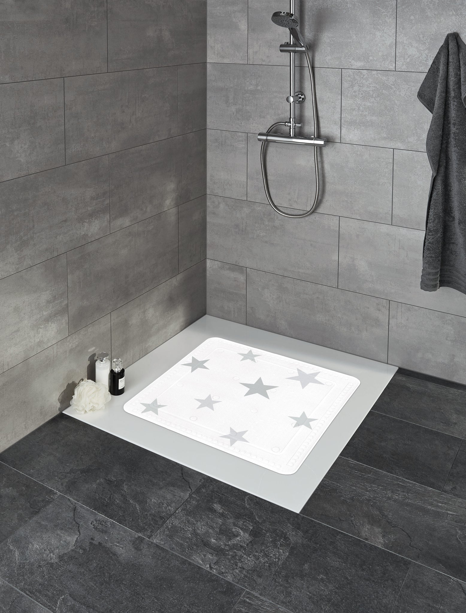Silbergraue Duscheinlage STARS 55 x 55 cm liegt in einer gefliesten Dusche mit Duscharmatur.