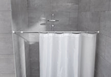 Eckdusche mit grauen Fliesen, weißem Duschvorhang und Brausekopf oben