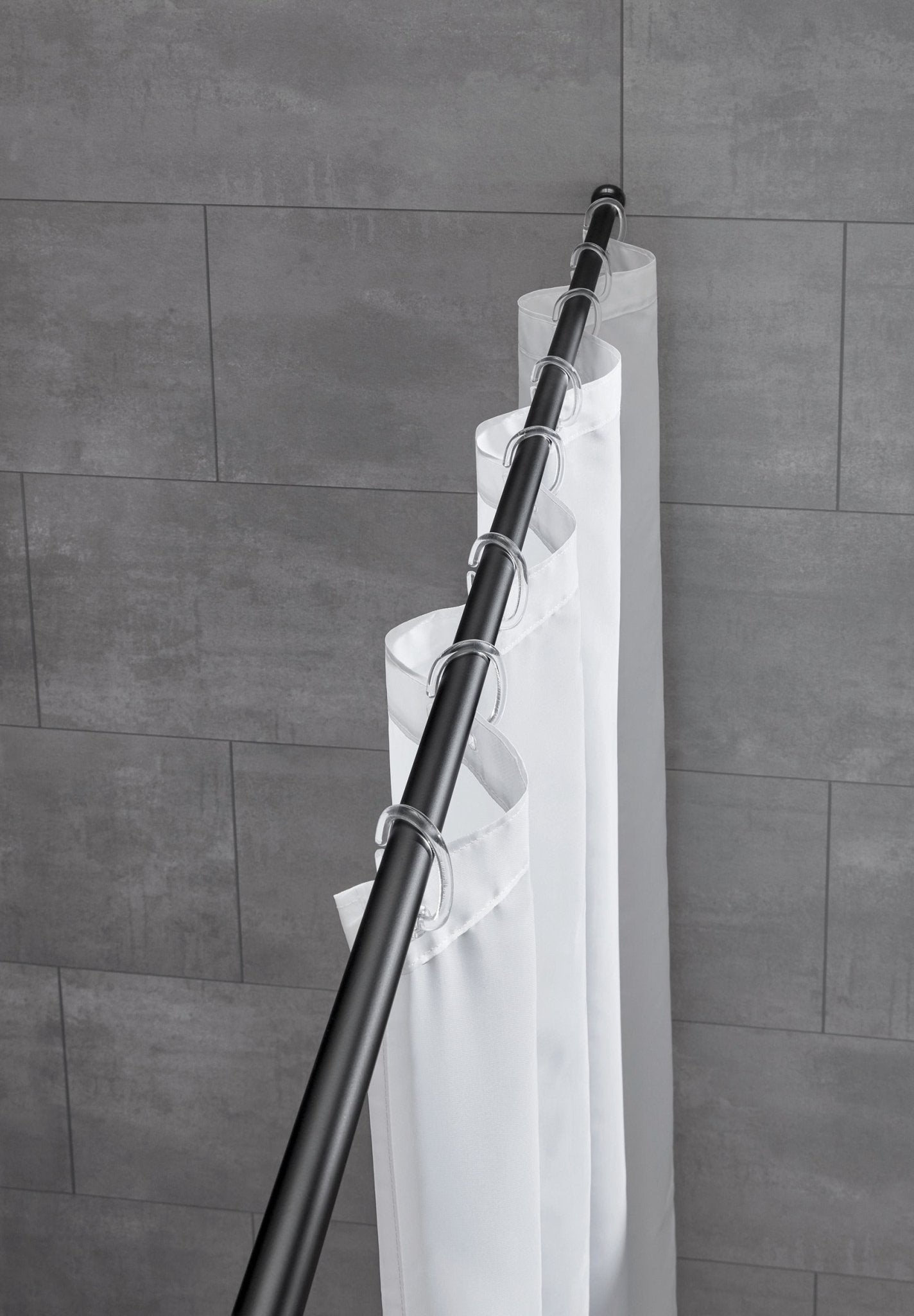 Schwarze Duschvorhang-Federstange hält weißen Vorhang vor grauer gefliester Badezimmerwand.