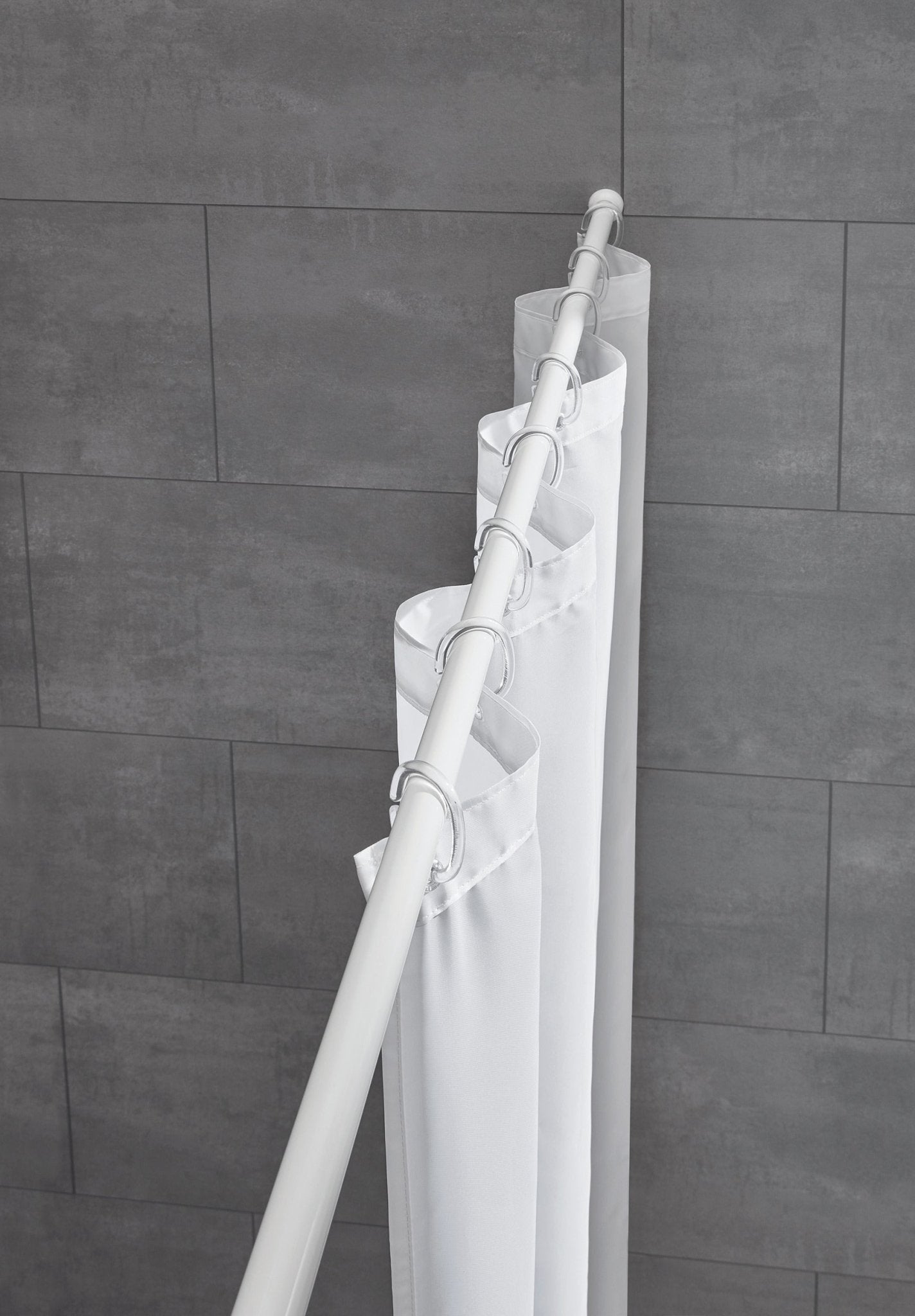 Weiße Duschvorhang-Federstange mit eingehängtem Vorhang vor grauen Fliesen im Bad.