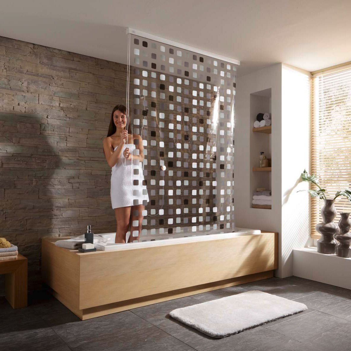 Frau in Badewanne nutzt grauen Duschvorhang für Duschrollo-Leerkassette 128 x 240 cm vor Steinwand.