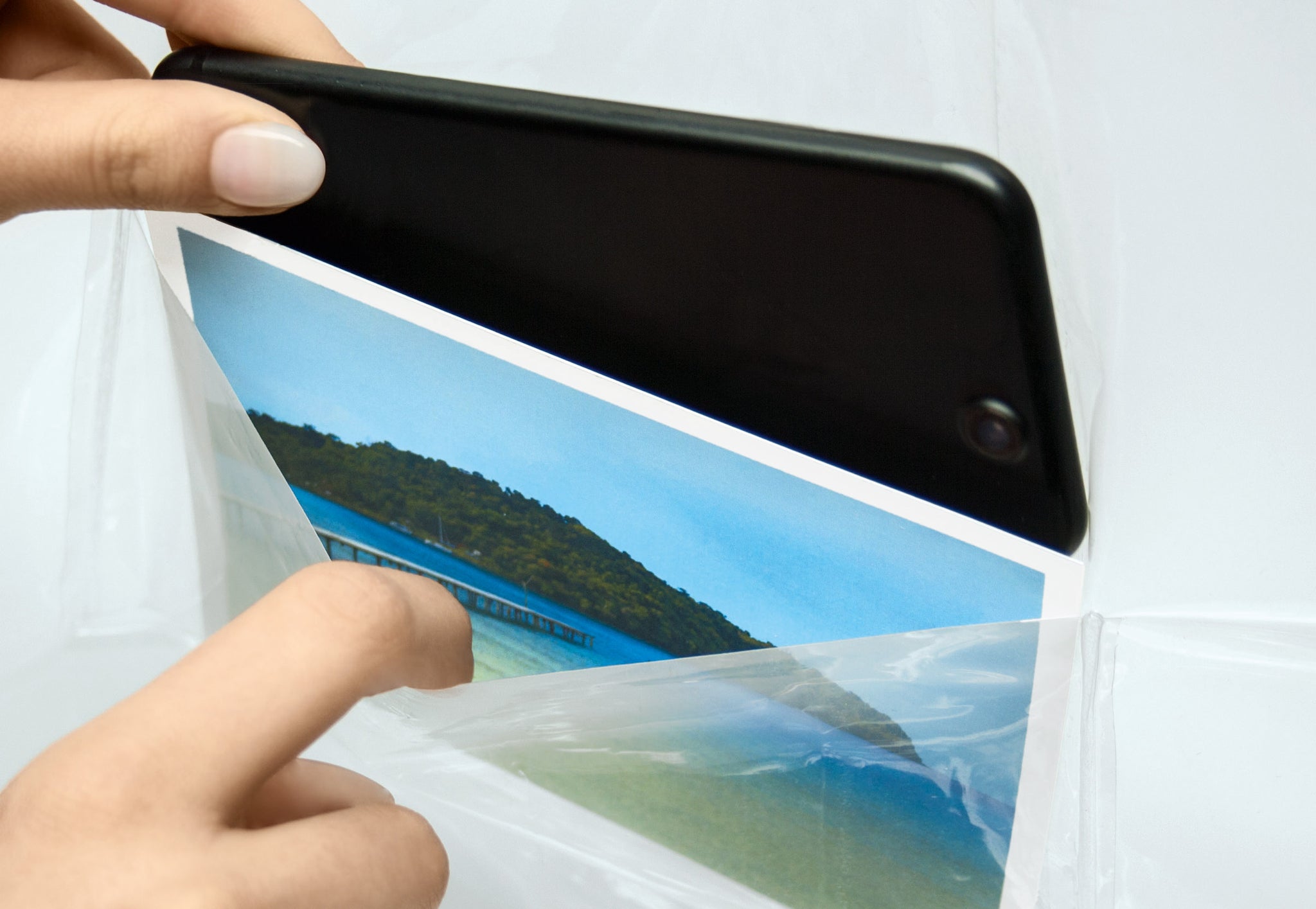 Hand steckt Foto und Smartphone in Tasche des Duschvorhangs PEVA POCKET Clear 180 x 200 cm.