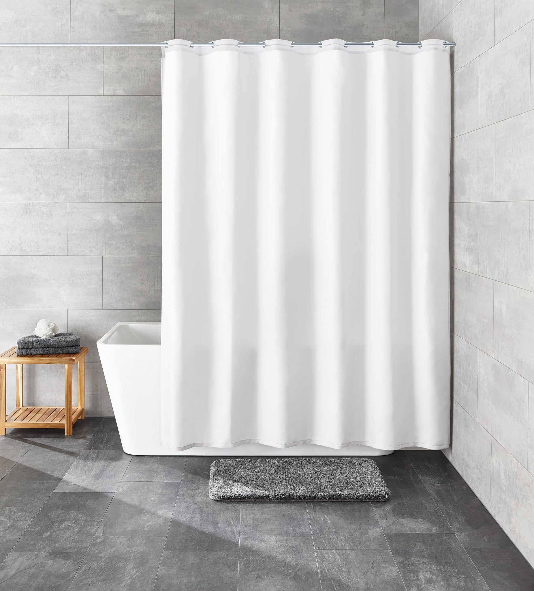 Weißer Duschvorhang vor Badewanne mit grauer Matte und Hocker aus Holz