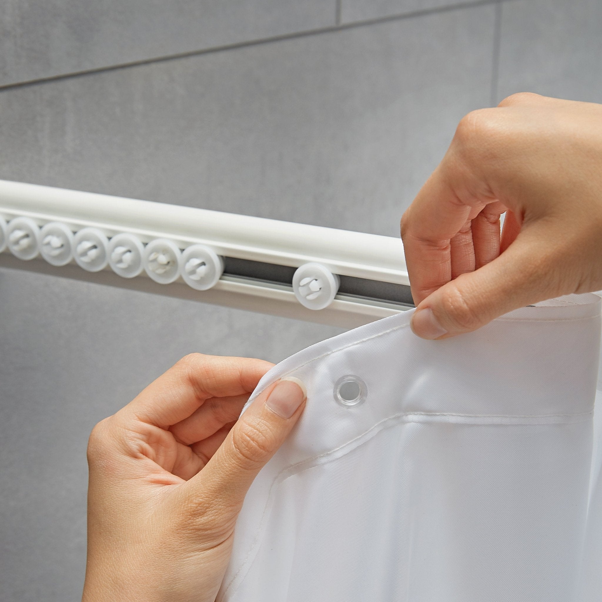 Hände befestigen weißen Duschvorhang an weißer Duschvorhang-Winkelschiene mit Gleitern im Bad.
