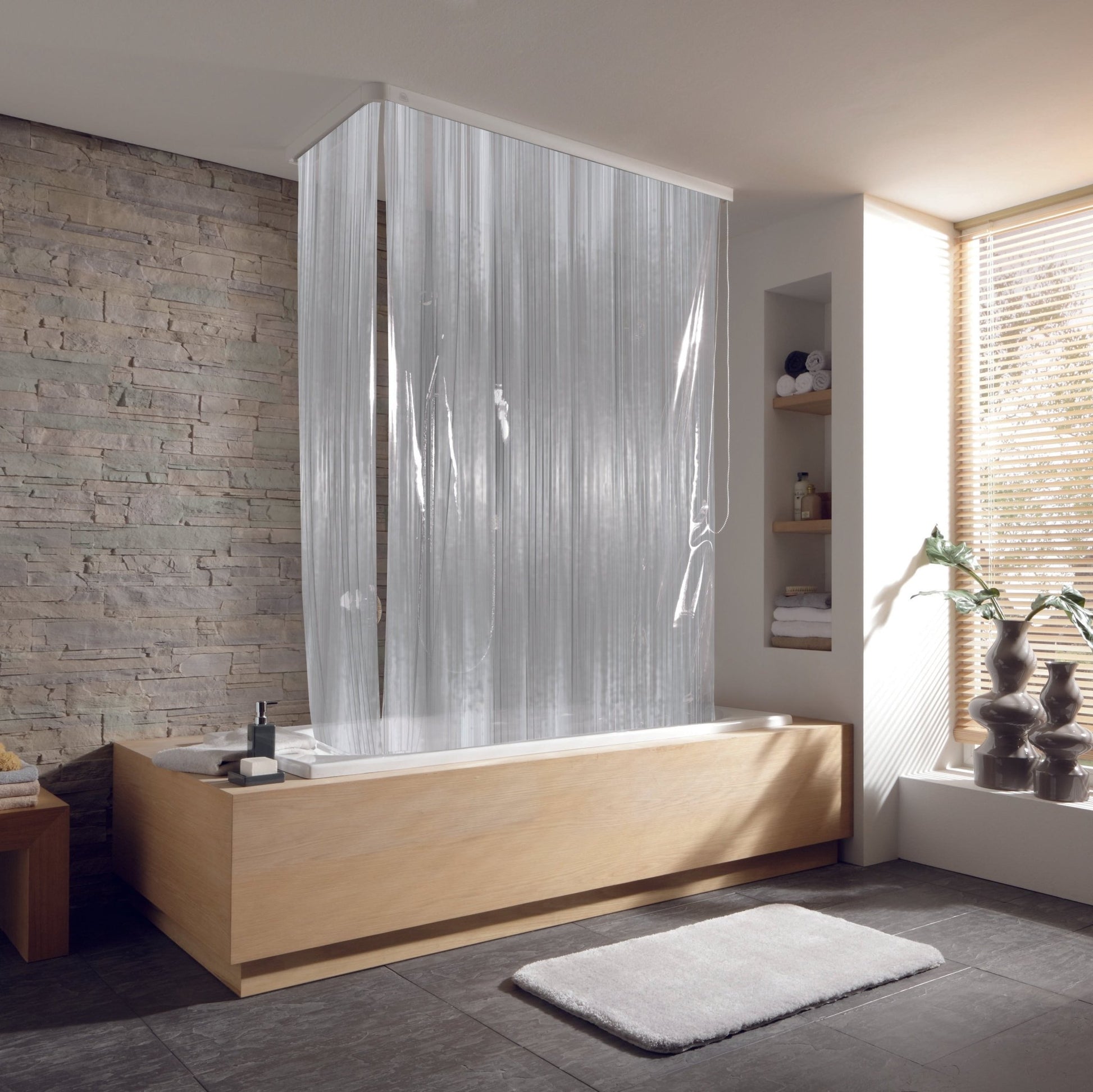 Eckduschrollo-Komplettset Milky an Badewanne in modernem Bad mit Steinwand und großem Fenster.