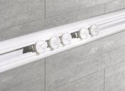 Weiße Duschvorhang-Winkelschiene mit Gleitern ist vor grauen Badezimmerfliesen montiert.