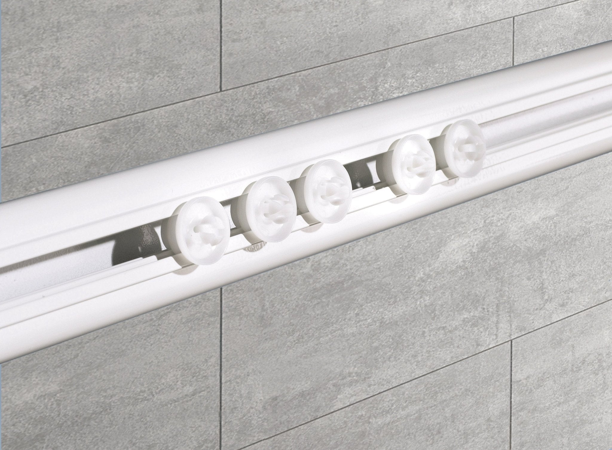 Weiße Duschvorhang-Winkelschiene mit Gleitern ist vor grauen Badezimmerfliesen montiert.