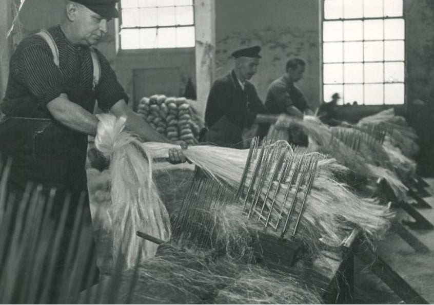 Historische Kleine-Wolke-Produktion 1924 mit Arbeitern, die Fasern an Maschinen kämmen.