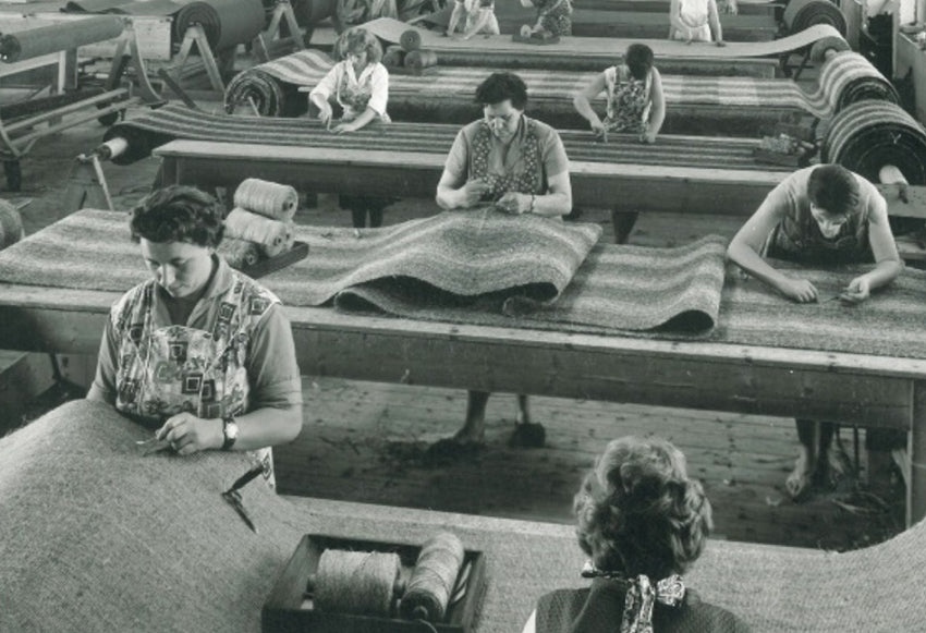 Historische Aufnahme von Frauen, die 1947 in einer Fabrik Teppiche von Hand bearbeiten.