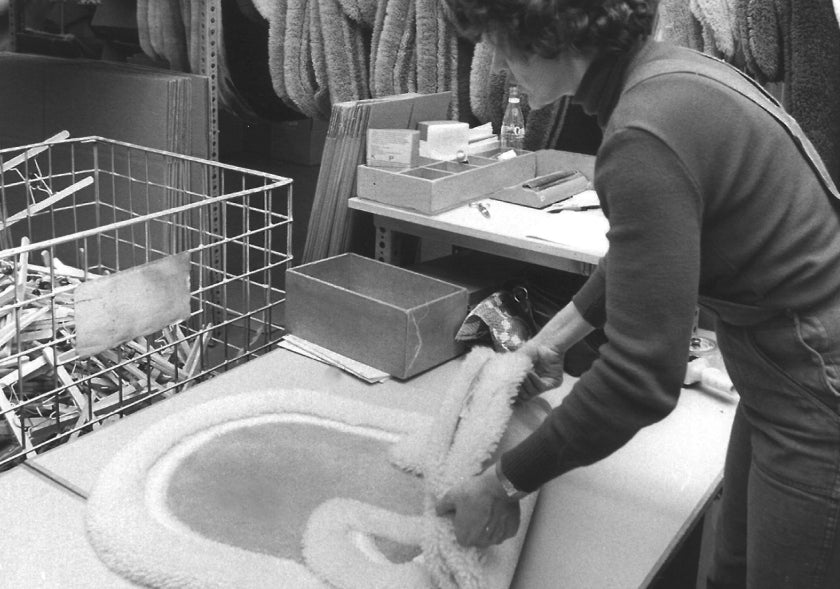 Frau in Werkhalle legt eine flauschige Badematte auf einen Arbeitstisch.