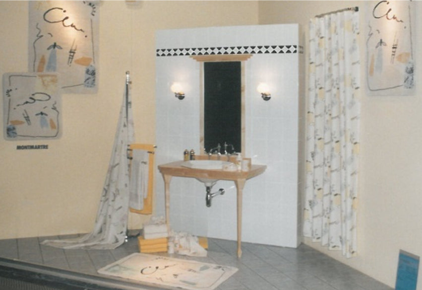 Badezimmer-Showroom mit Waschbecken, Spiegel, Duschvorhang und passenden Badteppichen im Montmartre-Dekor.