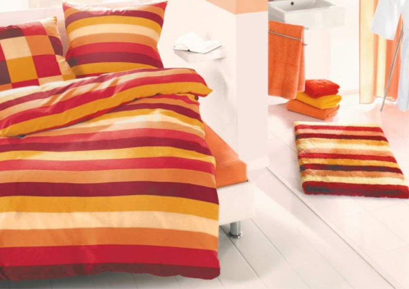 Kleine Wolke Bettwäsche mit roten und orangen Streifen und passenden Badtextilien im hellen Raum.