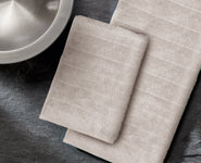 Zwei beige Handtücher auf dunkler Steinfläche neben Metallschale