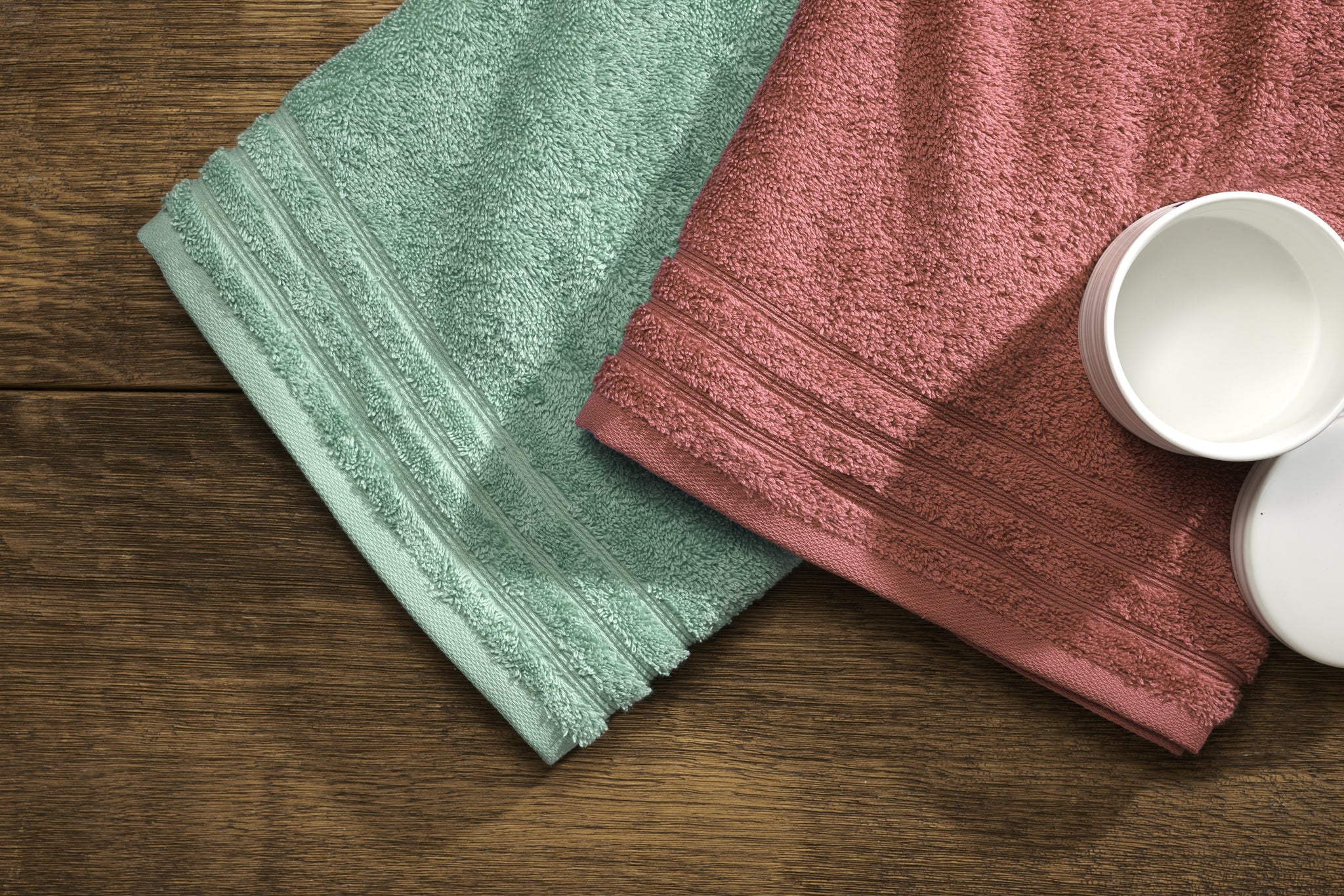 Frottier Handtuch ROYAL Maledivia 50x100 cm in Grün und Rosa neben Cremedose auf Holztisch.