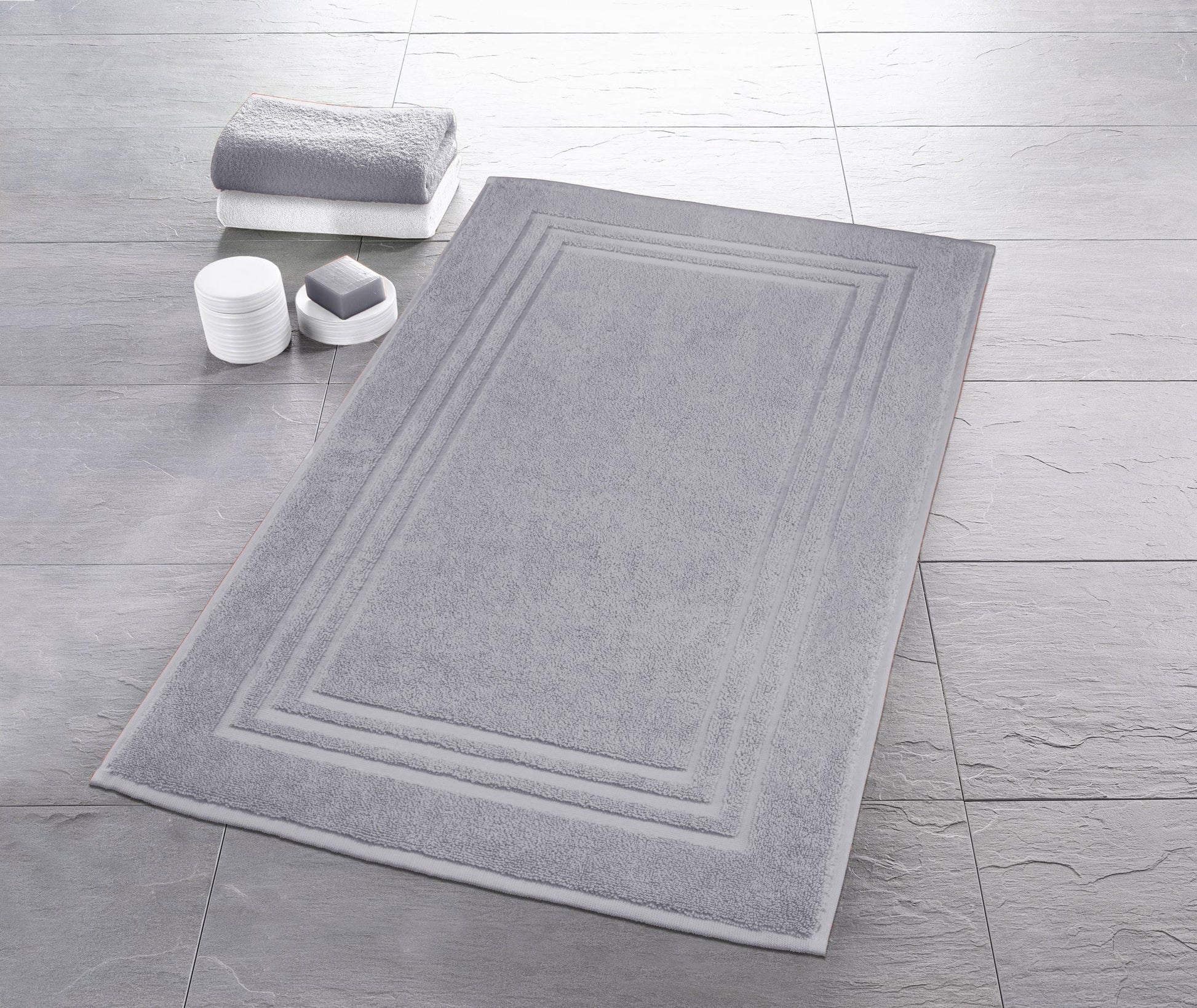 Graue rechteckige Badematte auf Fliesenboden mit Handtuch und Seife