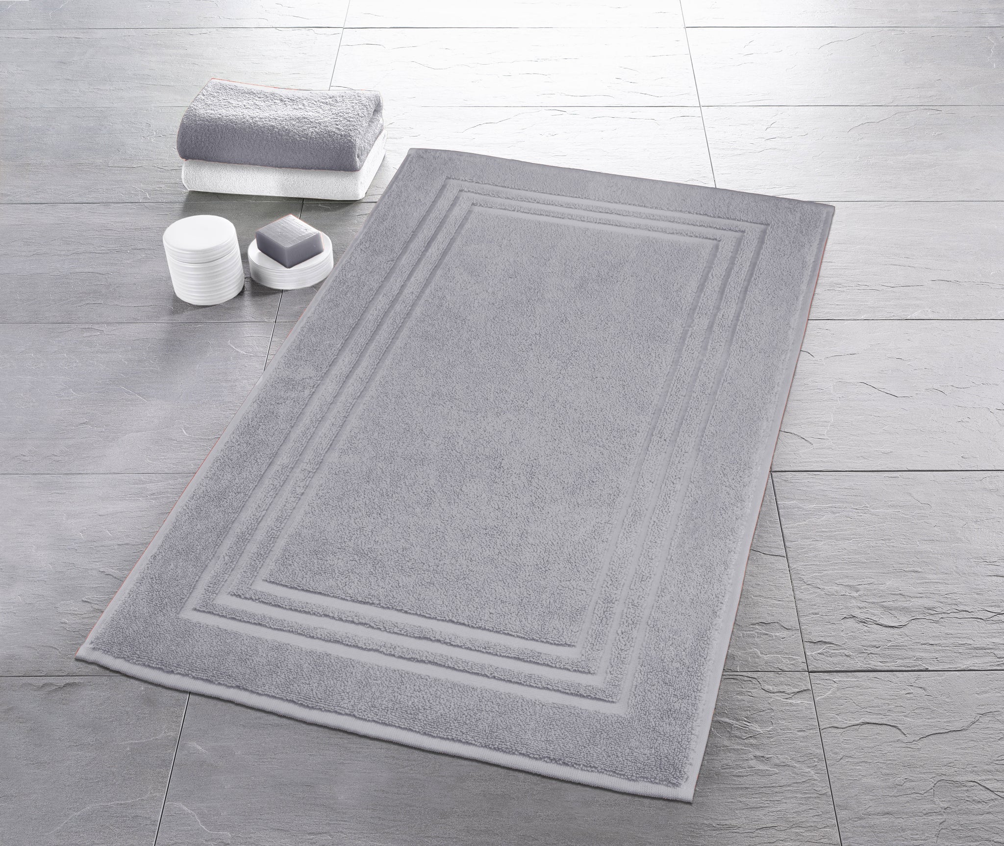 Graue rechteckige Badematte auf Fliesenboden mit Handtuch und Seife