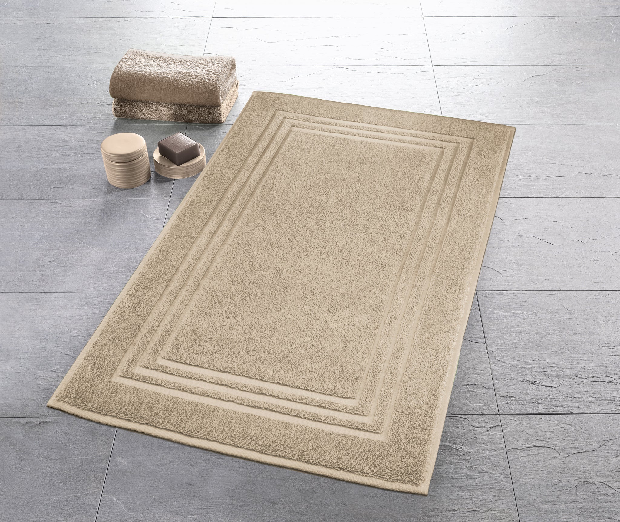 Beiger Badematte auf grauem Fliesenboden mit Handtuch und Seifenspender