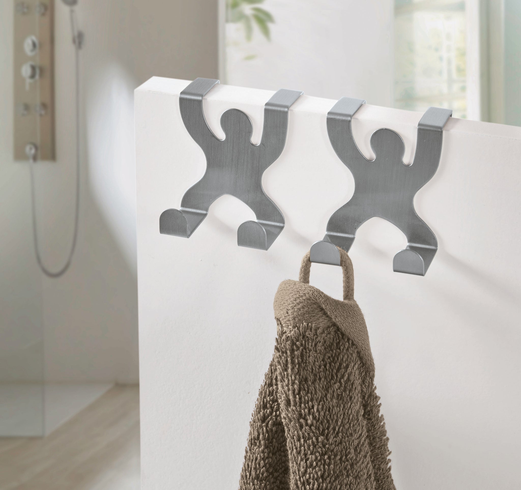 Zwei silberne Handtuchhaken in Menschenform mit braunem Handtuch