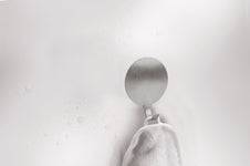 Runder Edelstahl-Handtuchhaken an weißer Wand mit weißem Handtuch