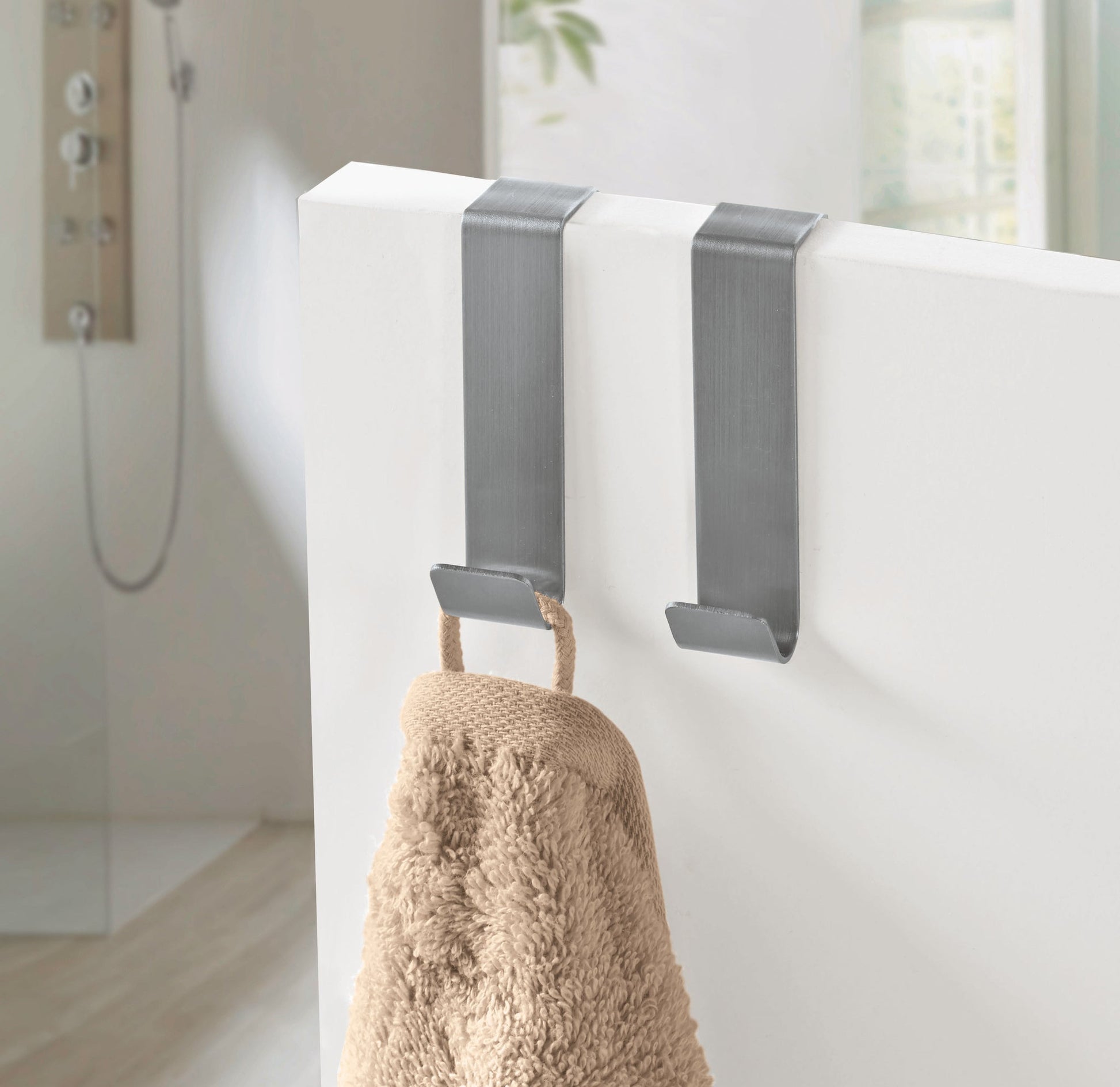 Zwei silberne Türhaken aus Metall mit hängendem beigem Handtuch