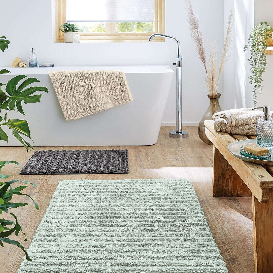 Helles Bad mit freistehender Wanne und drei flauschigen Badematten