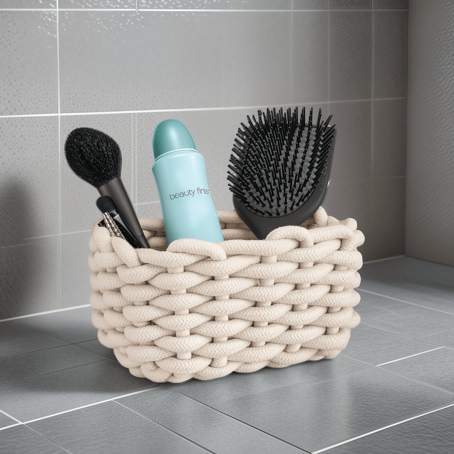 Geflochtener cremefarbener Badezimmerkorb mit Haarbürste, Puderpinsel und Deospray auf grauer Fliese.