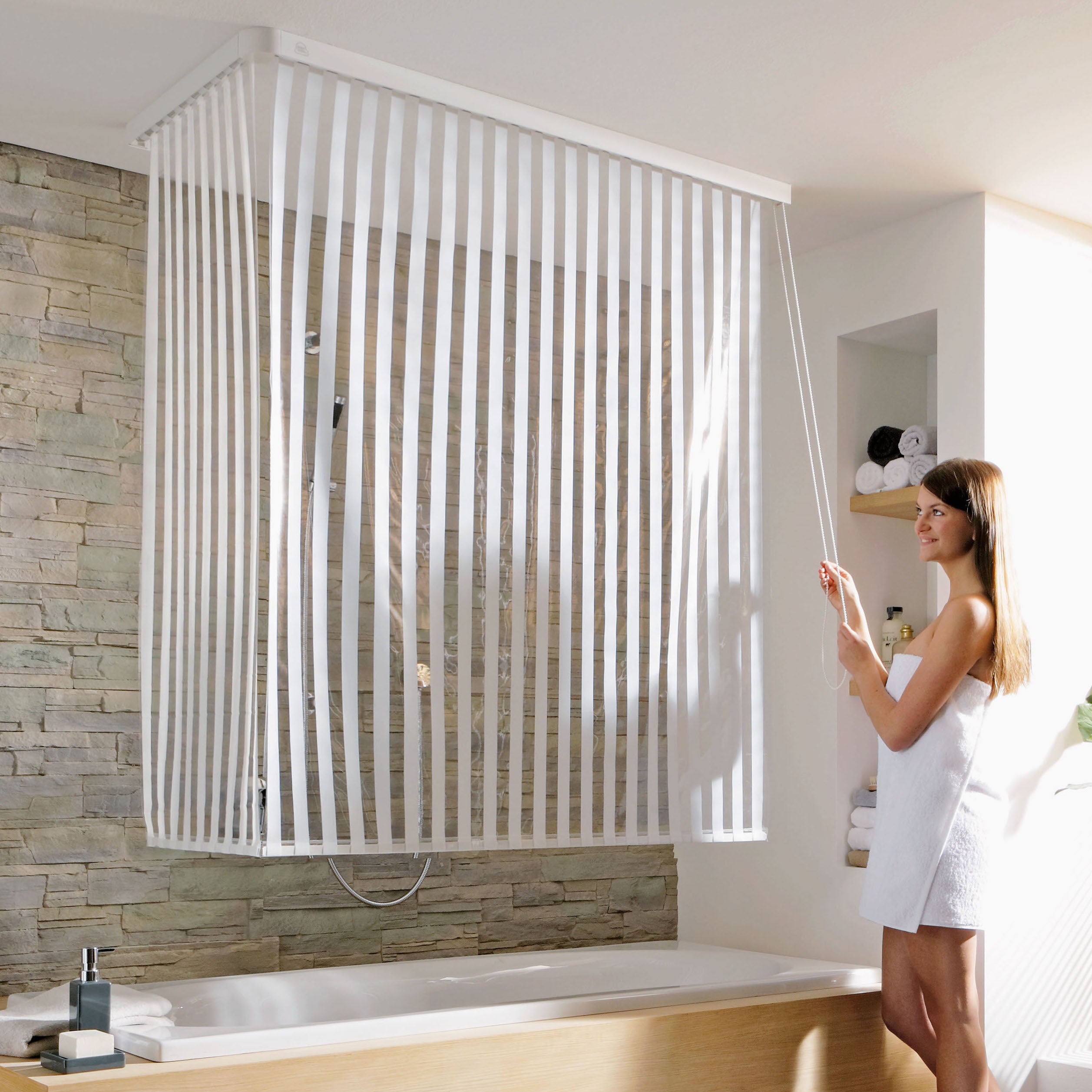 Frau zieht weißes Kleine Wolke Duschrollo mit Streifen über einer Badewanne im modernen Bad zu.