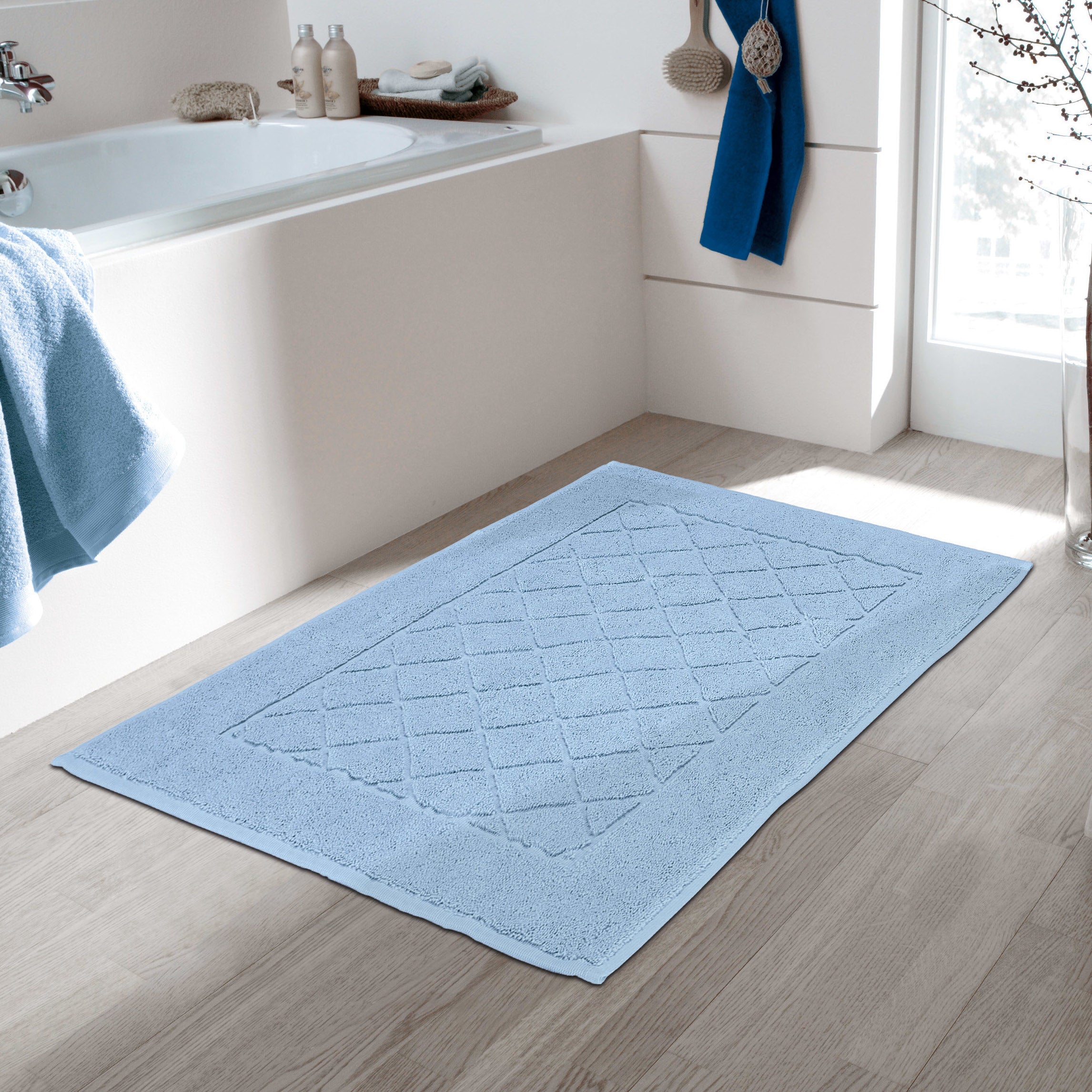 Hellblauer Kleine Wolke Frottier Badvorleger liegt vor der Badewanne in einem modernen, hellen Badezimmer.