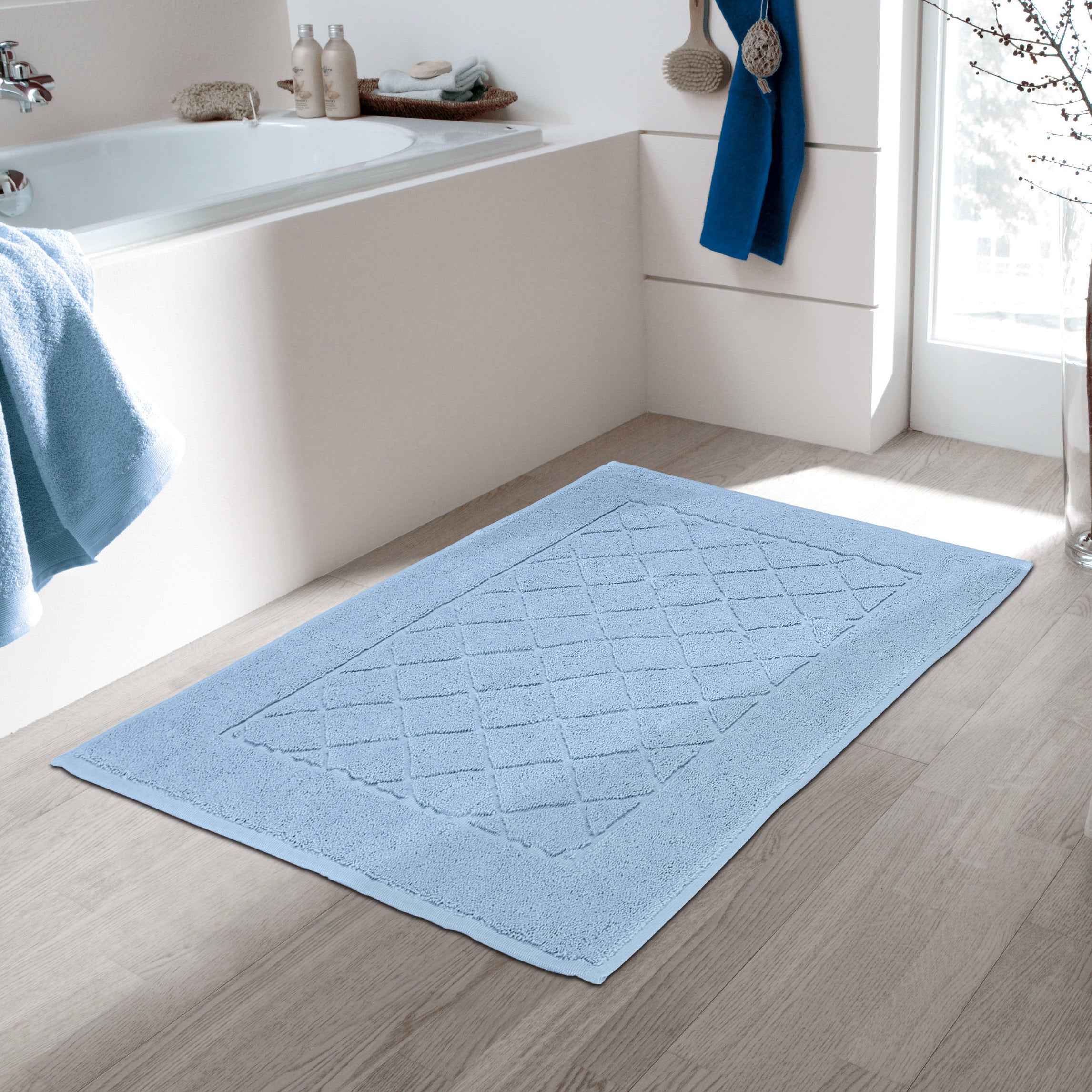 Hellblauer Frottiervorleger von Kleine Wolke liegt vor einer weißen Badewanne im modernen Badezimmer.