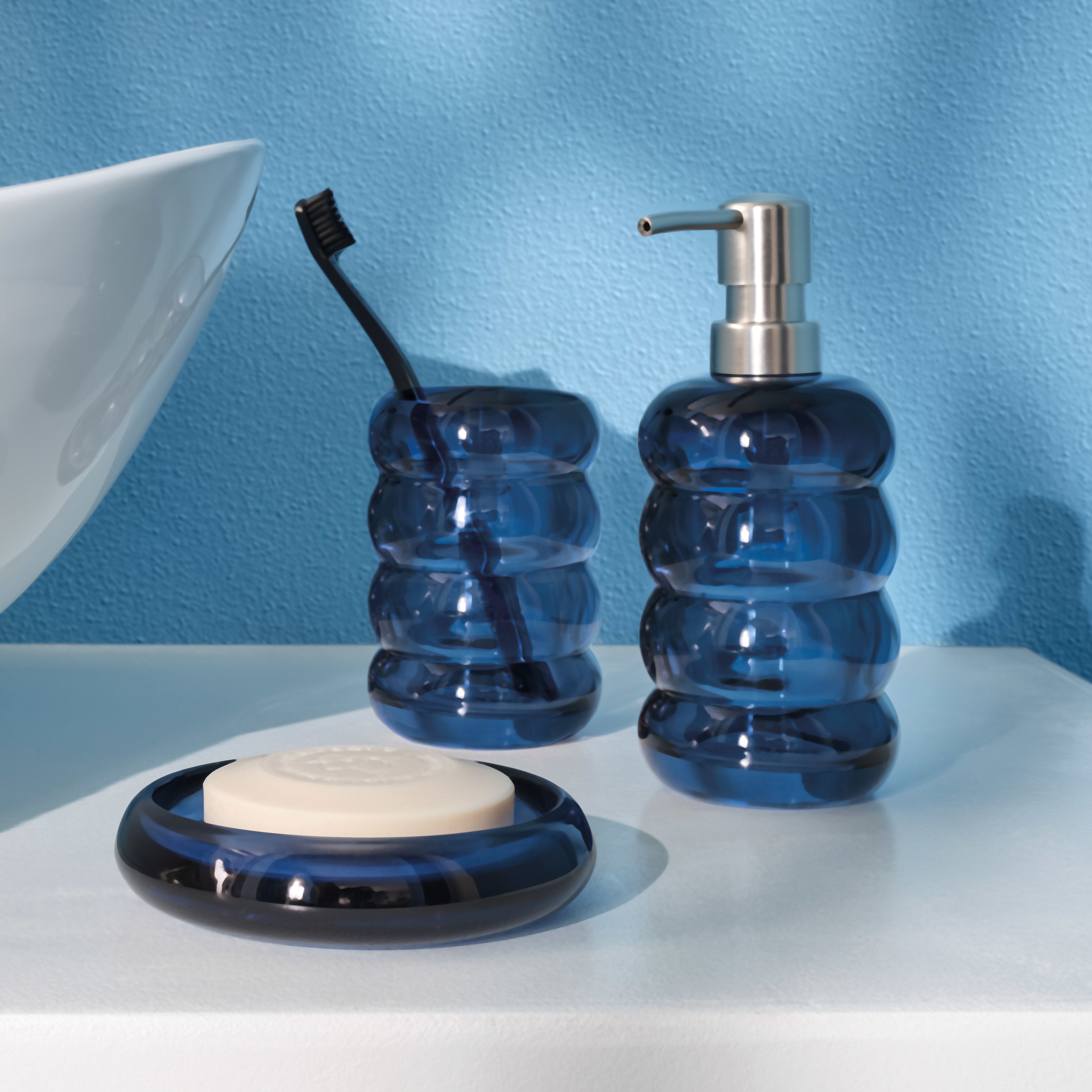 Blaue Badaccessoires mit Seifenspender, Zahnputzbecher und Seifenschale auf weißer Ablage.