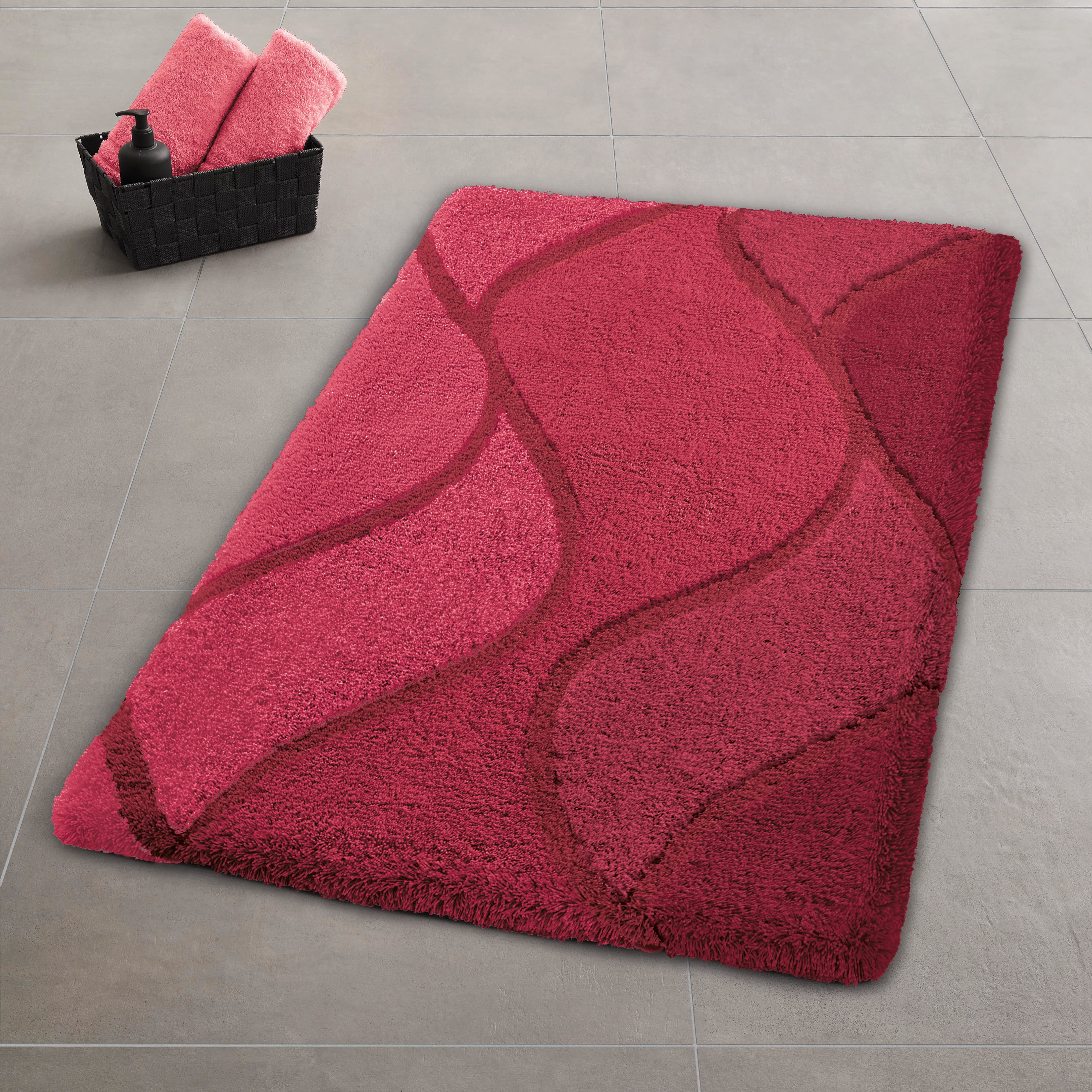 Rote Badematte mit Wellenmuster auf grauen Fliesen neben schwarzem Korb mit Handtüchern.