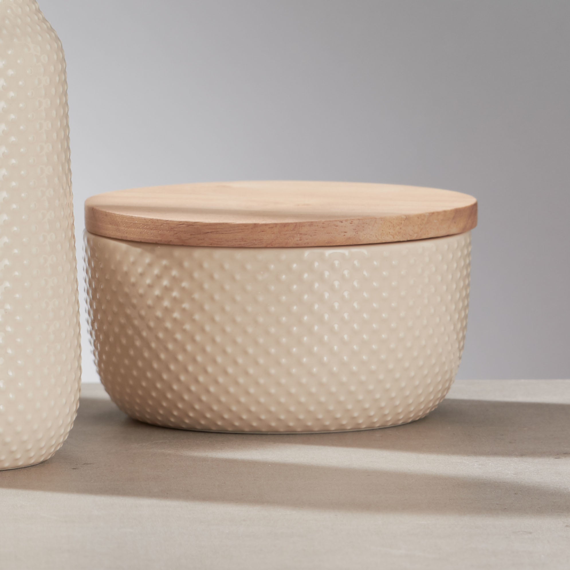 Beige Kleine Wolke Wattedose mit Holzdeckel auf Betonfläche neben passendem Spender.