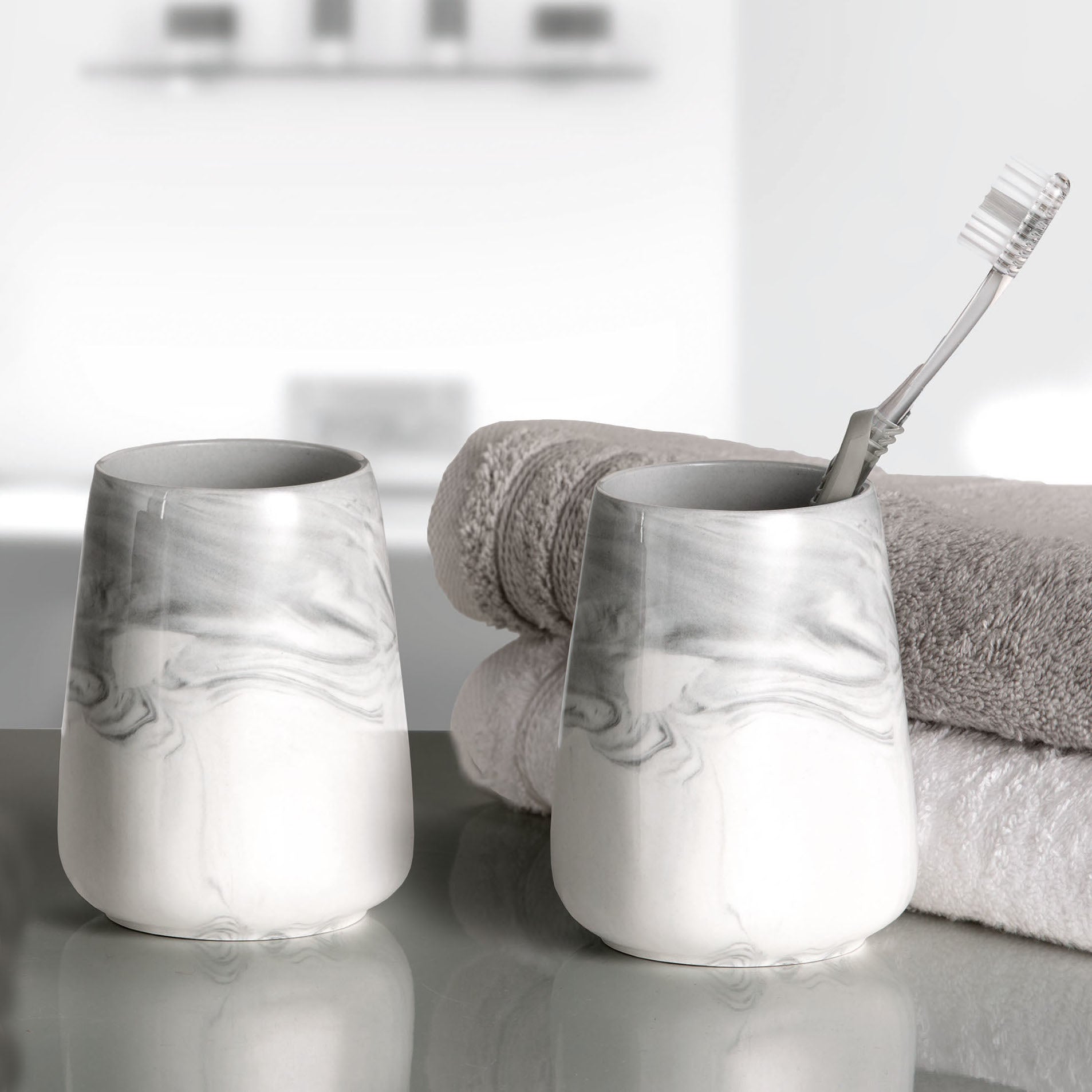 Zwei Kleine-Wolke-Zahnputzbecher in Marmoroptik mit Handtüchern und Zahnbürste im Bad.