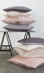 Gestapelte Kopfkissen in Grau, Rosa und Creme auf und vor Tisch
