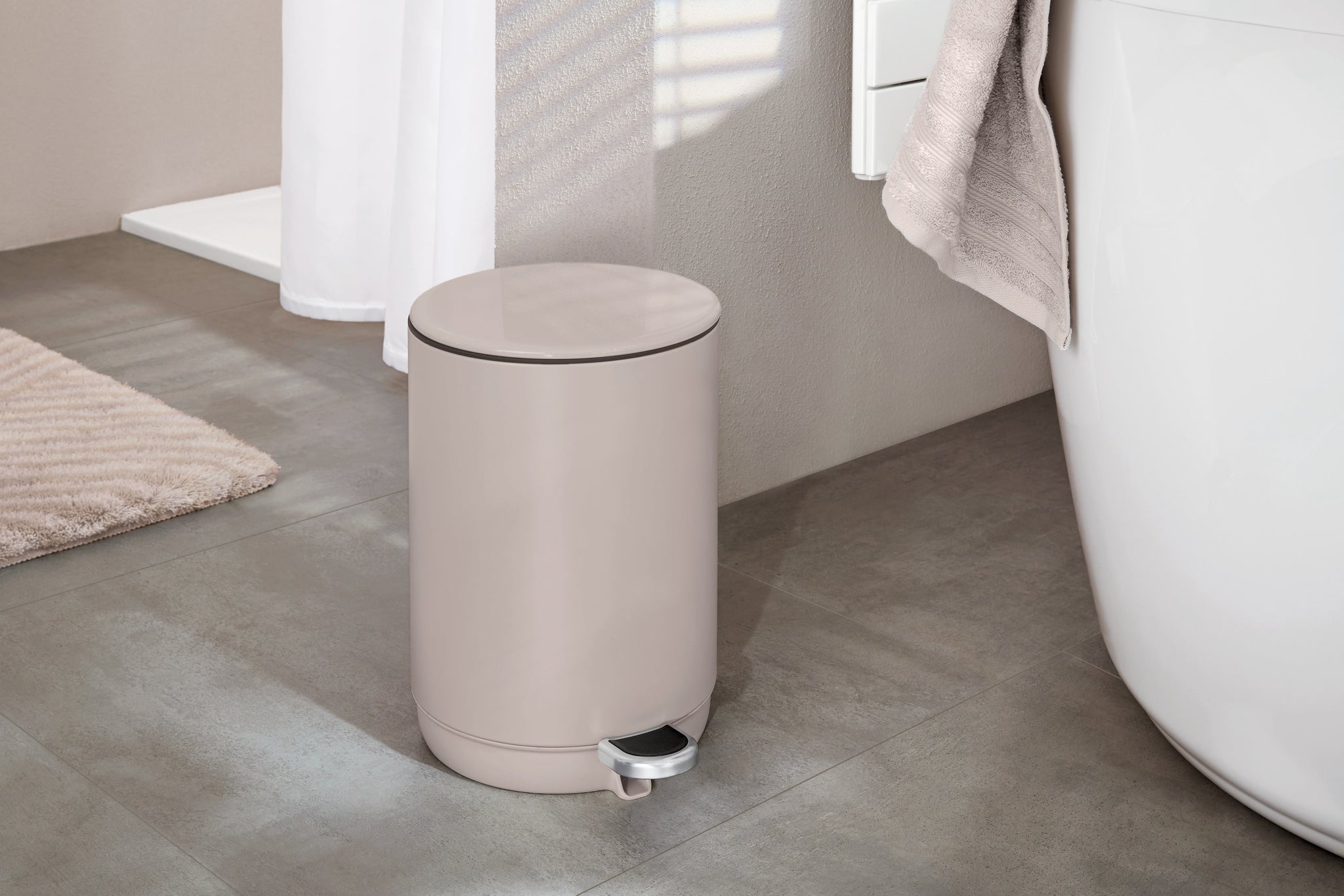 Beiger Treteimer im modernen Badezimmer neben Badewanne und Matte