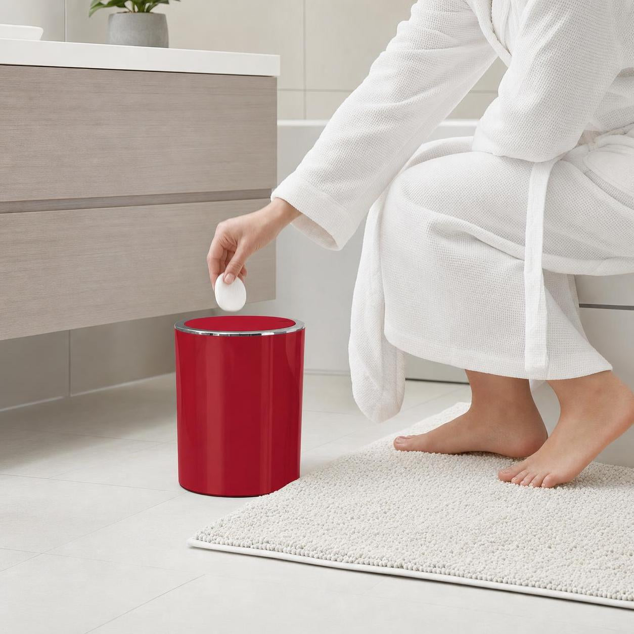 Eine Person wirft ein Wattepad in einen roten Badmülleimer.