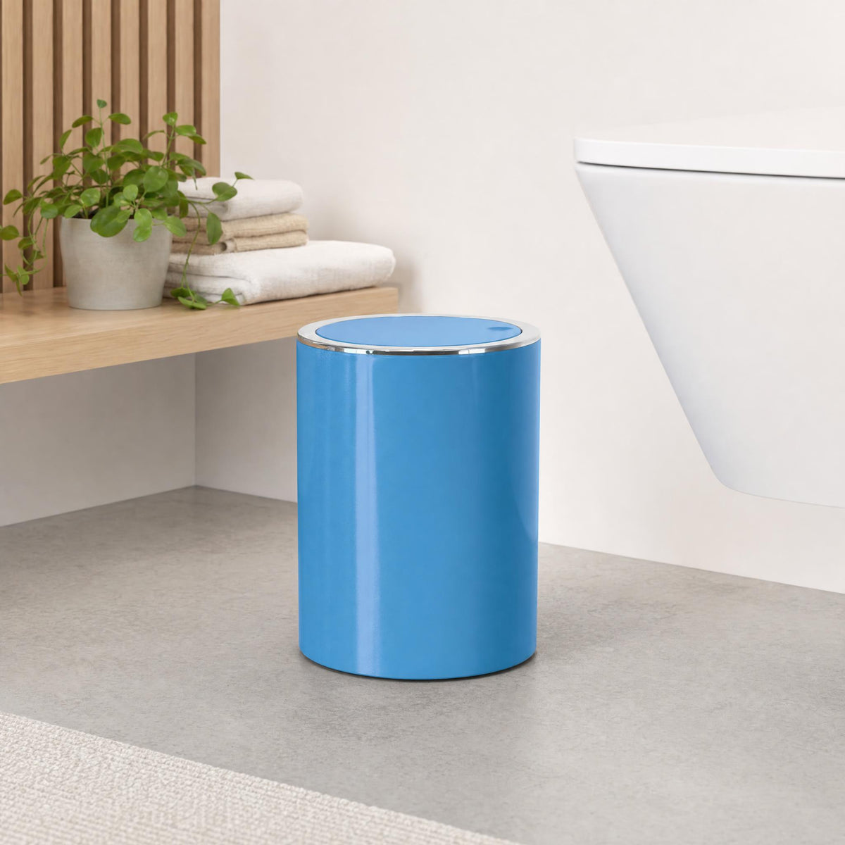 Blauer Badezimmereimer neben WC, Handtüchern und Zimmerpflanze.