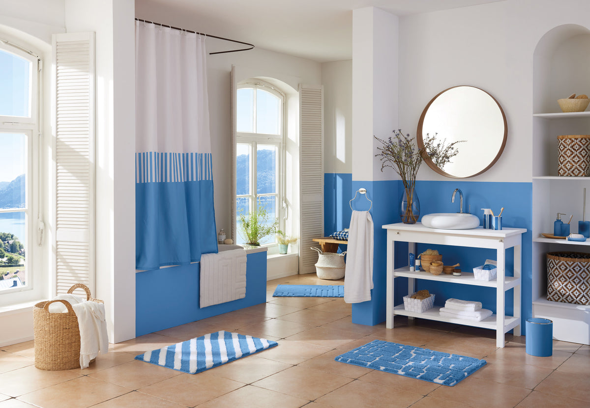 Helles Bad mit blauen Textilien, Waschtisch und Dusche am Fenster.