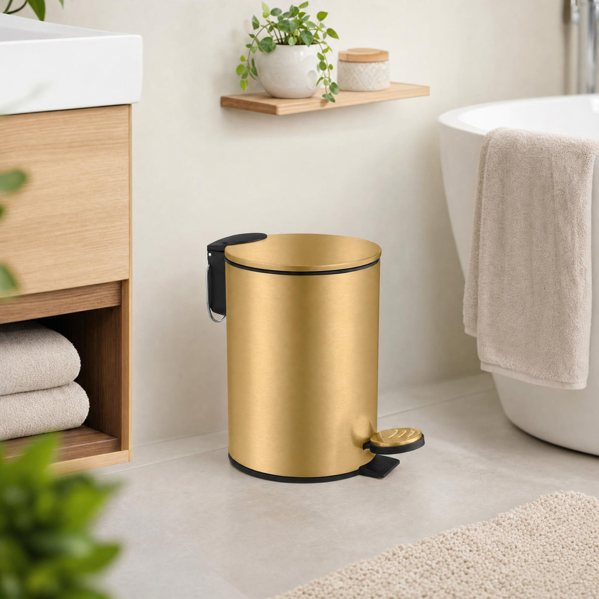 Goldfarbener Treteimer im hellen Badezimmer neben Badewanne und Holzwaschtisch.