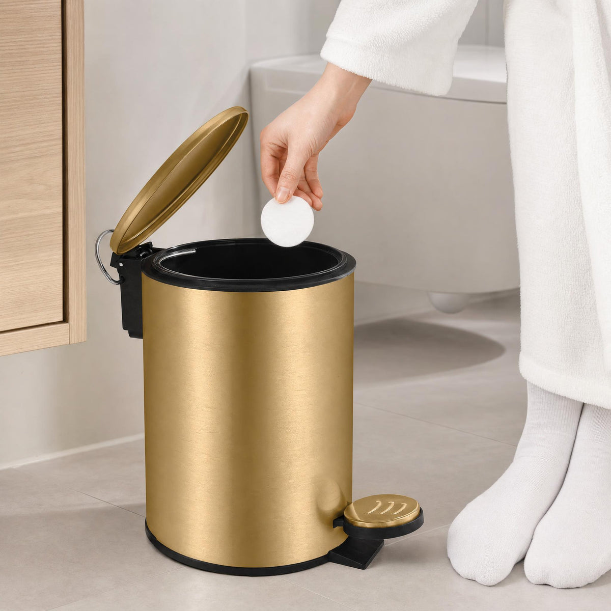 Goldfarbener Kosmetikeimer im Bad, Hand wirft Wattepad in den offenen Eimer.