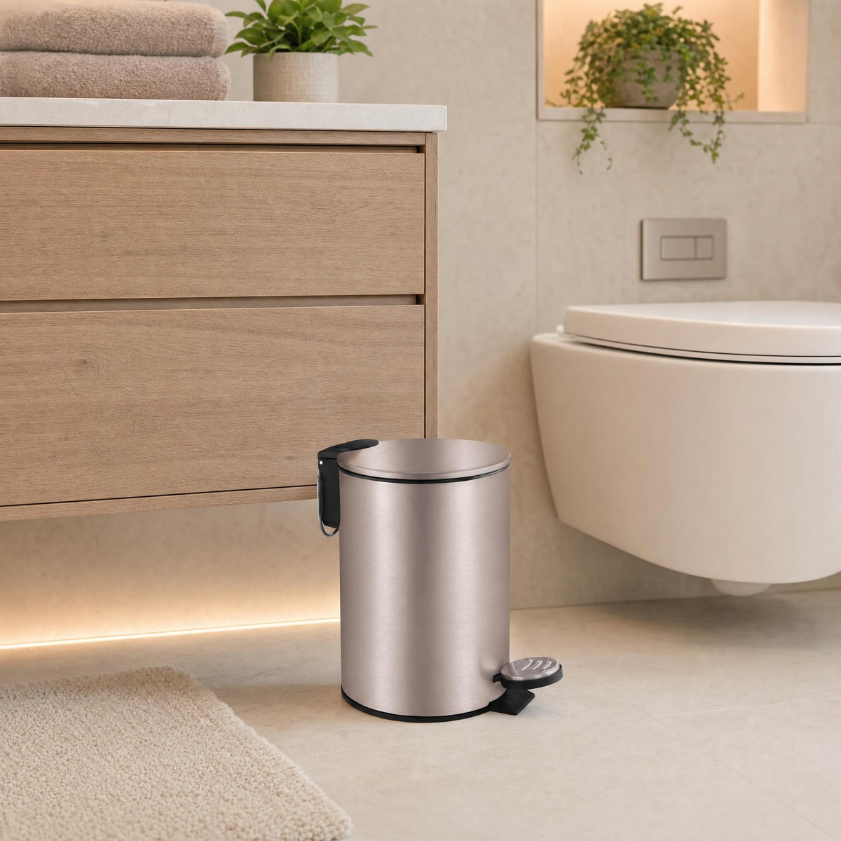 Silberfarbener, matter Treteimer im Badezimmer neben Holzunterschrank und WC.