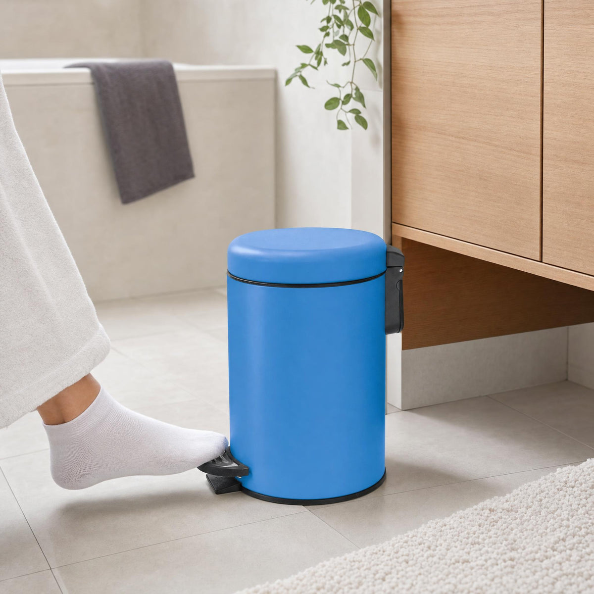 Blauer Treteimer im Bad neben Holzschrank und Badewanne.