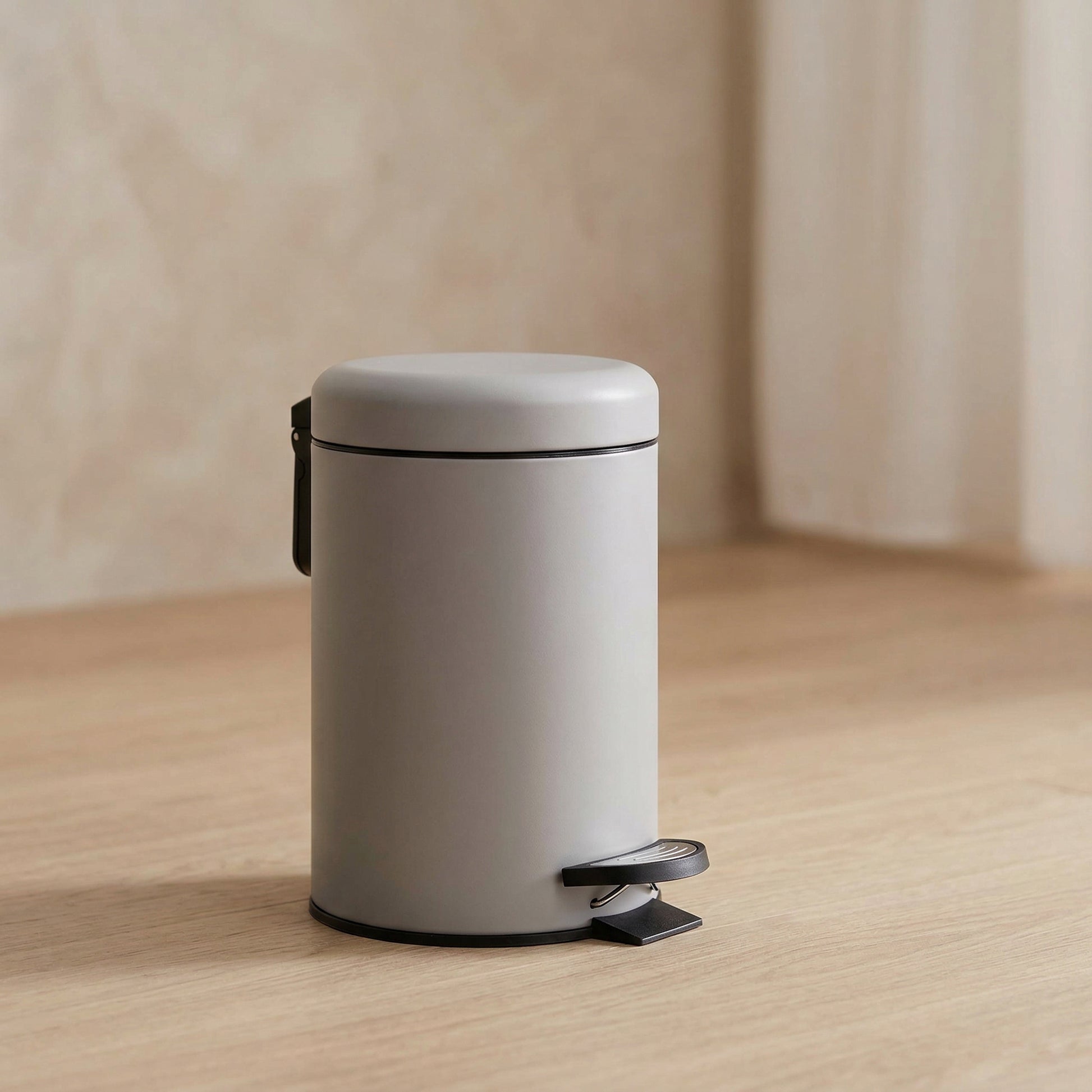 Kleiner, zylindrischer, hellgrauer Treteimer auf hellem Holzboden stehend