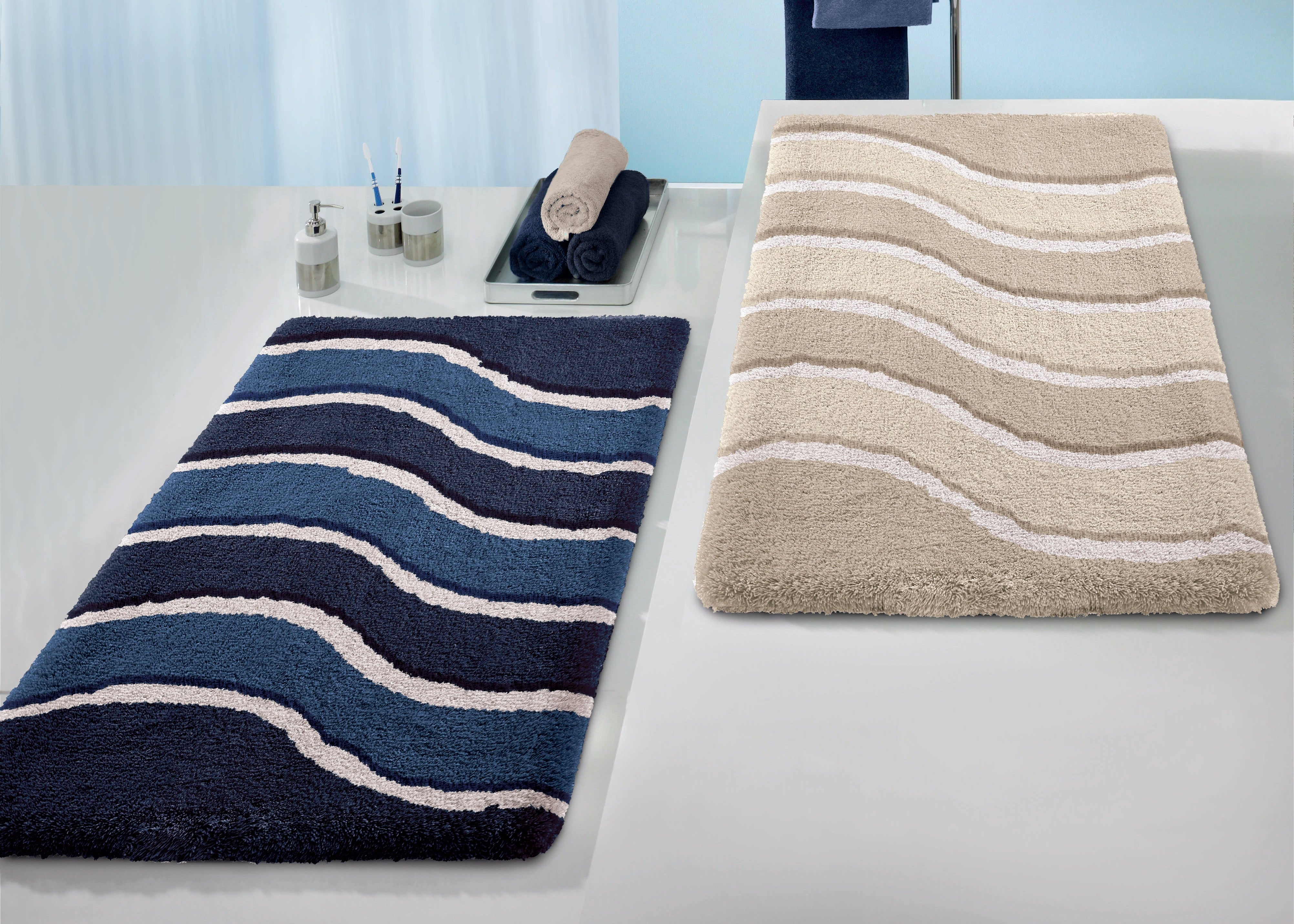 Flauschige Badteppiche in Blau und Beige mit weißen Wellen liegen im Bad.