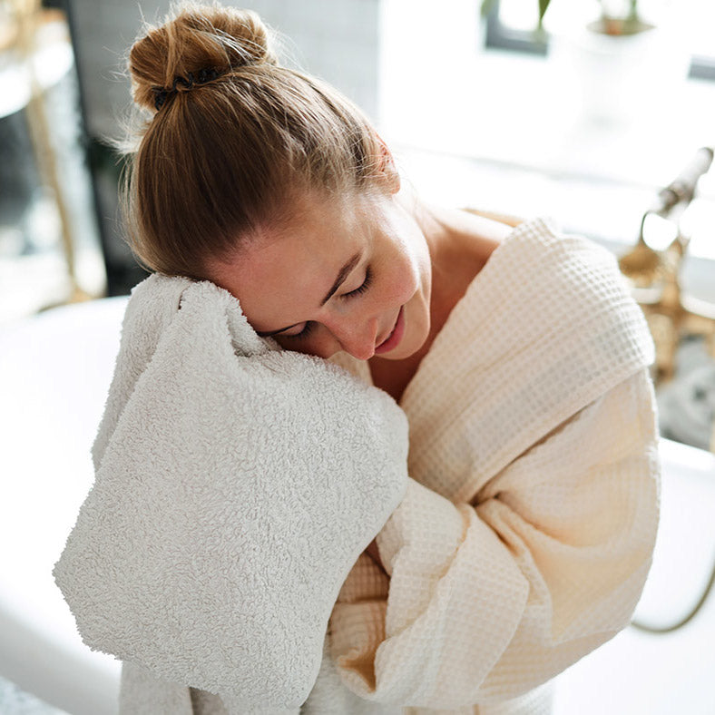 Frau im Bademantel trocknet Gesicht mit weichem, nachhaltigem Kleine Wolke Handtuch im Bad.