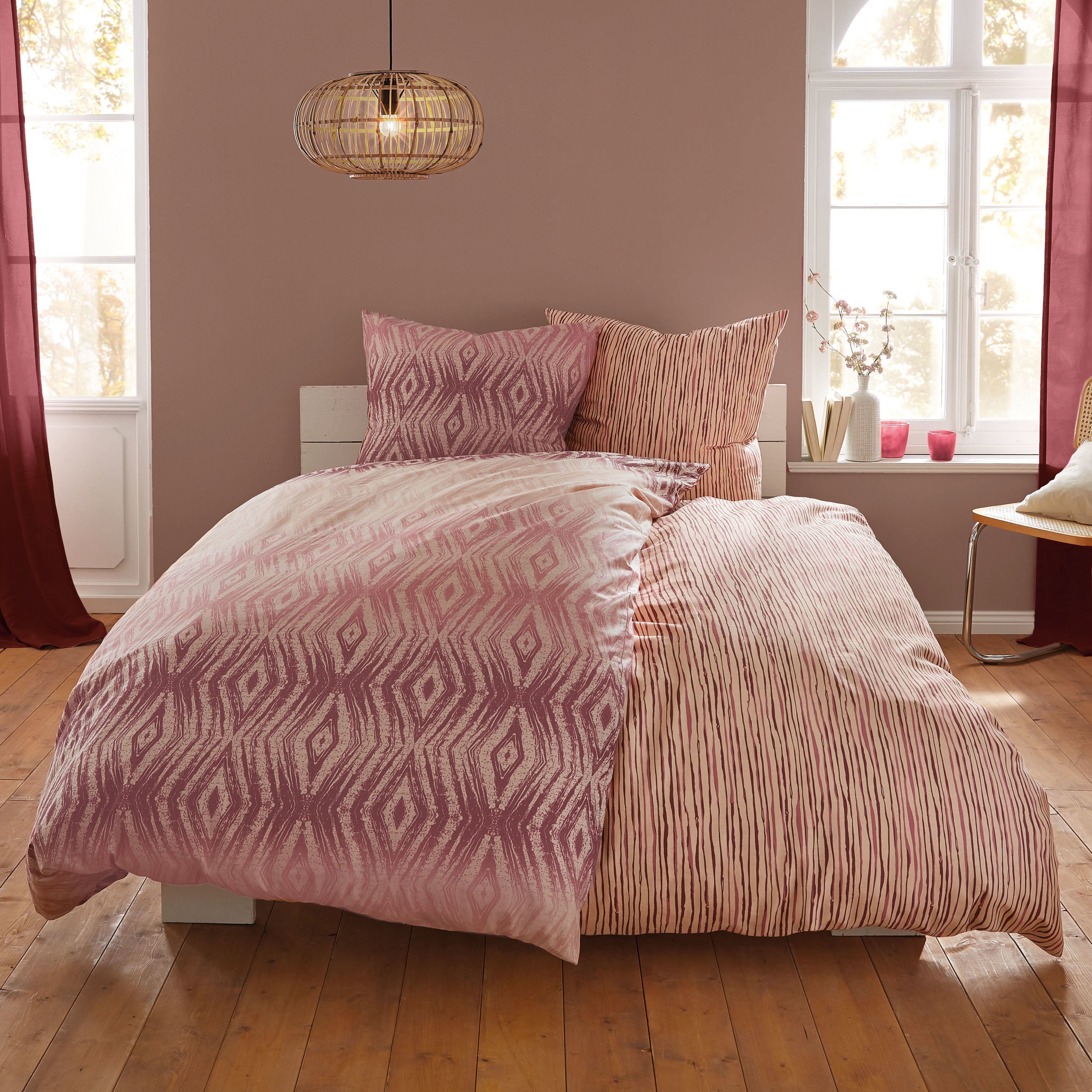 Rosa Kleine-Wolke-Bettwäsche mit grafischem Muster liegt auf einem Bett in einem hellen Schlafzimmer.