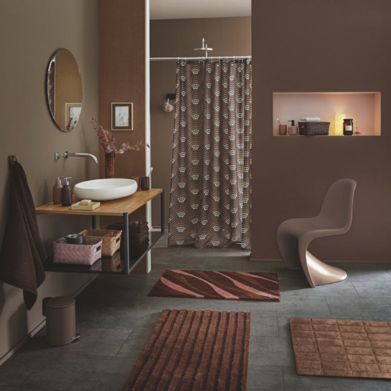 Modernes Bad mit braunen Badteppichen, gemusterter Duschvorhang und Designstuhl in Beige.