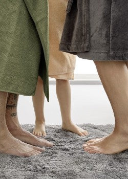 Füße von zwei Erwachsenen und einem Kind auf flauschigem Badteppich